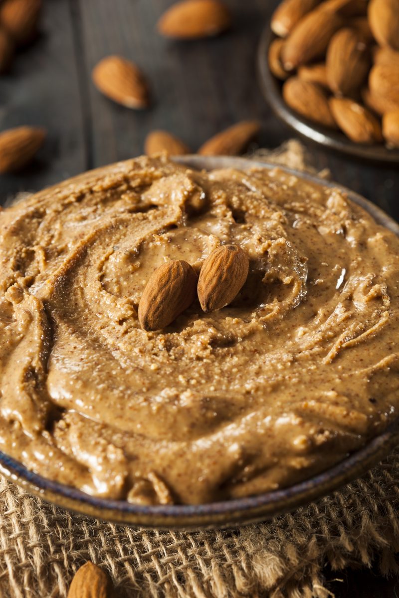 Gros plan d’un bol d’amlou onctueux avec deux amandes entières au centre, ambiance bois sombre.