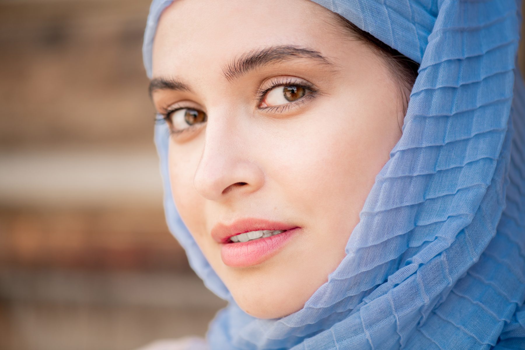 Portrait rapproché d’une femme portant un voile bleu texturé, regard doux, lumière naturelle.